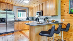 A modern kitchen with wooden cabinets, stainless steel appliances, a central island with bar stools, and a large window providing natural light.