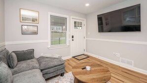 A living room with a grey sectional sofa, a wooden coffee table, a flat-screen TV mounted on the wall, and a door with a window. - Valley Ridge Retreat - For 8 (Cincinnati)