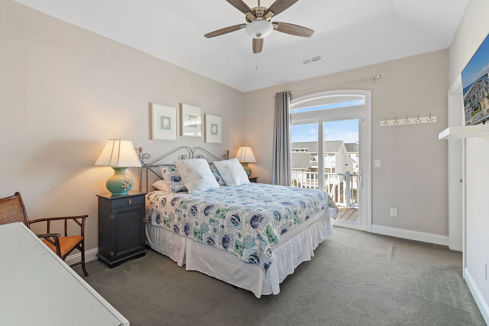 A bedroom with a bed, two bedside lamps, a chair, a ceiling fan, and a view of the outside.