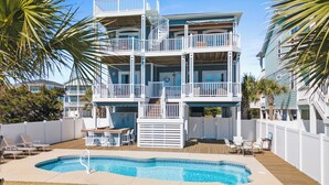 A multi-story building with a pool, outdoor seating, and a fenced deck. - Shrimply The Best -Luxury Holden Beach Home with Private Saltwater Pool, Elevator & Tiki Bar (Holden Beach)