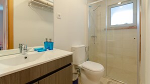 Une salle de bain avec un lavabo blanc, des distributeurs de savon bleus, des toilettes et une douche fermée par une paroi de verre.