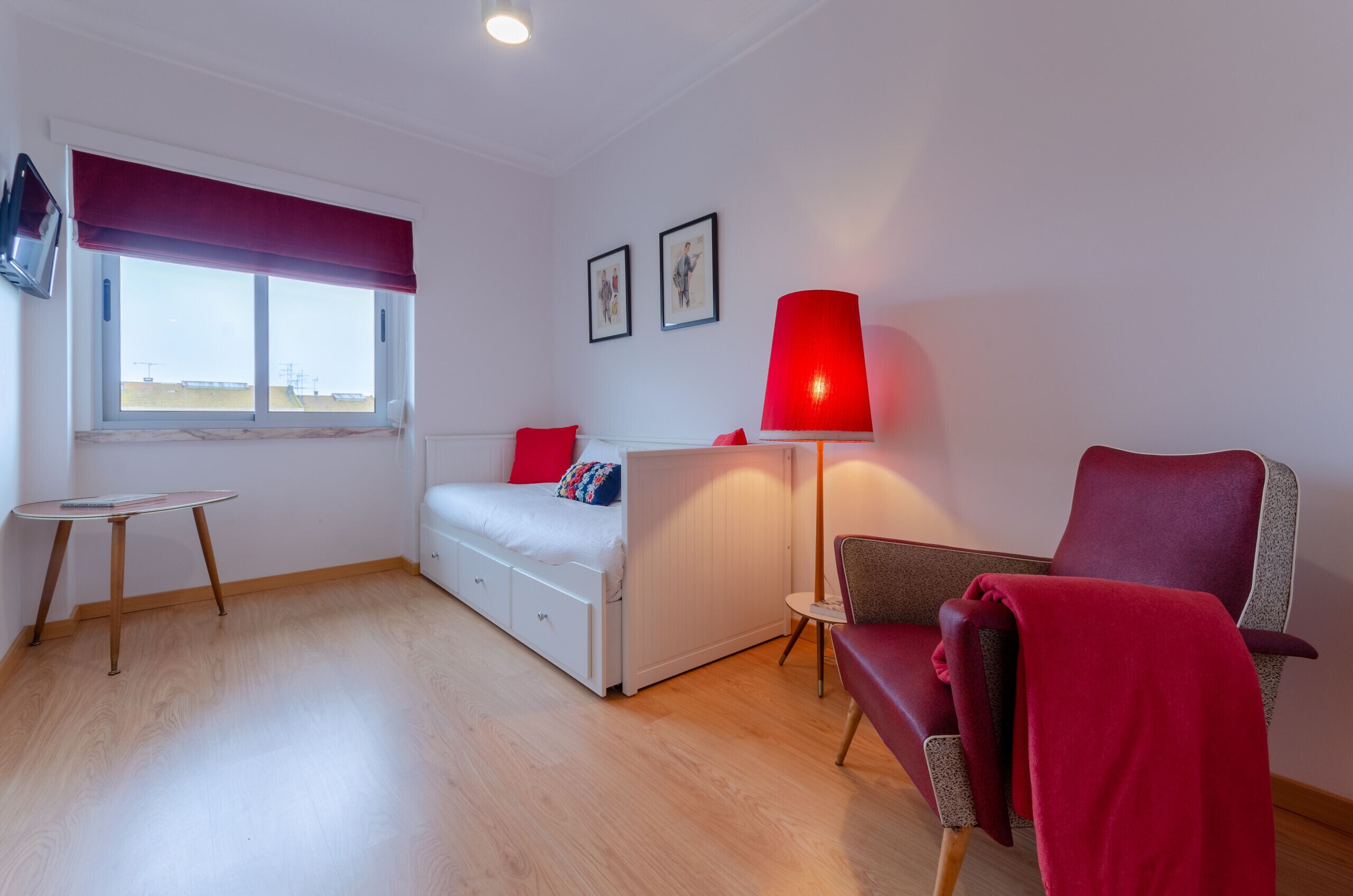 Une petite pièce comprenant un lit, une chaise rouge, une petite table et une fenêtre donnant sur un paysage agréable.