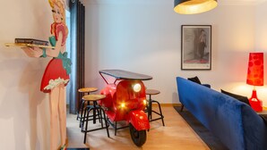 Un coin repas avec un scooter rouge, un canapé bleu, un luminaire suspendu et un tableau accroché au mur.