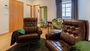 A room with two brown leather armchairs, a green armchair, a wooden door, a mirror, a window with curtains, and a small table with a chair. - Setubal Boutique Apartments III by Homing (Setubal)