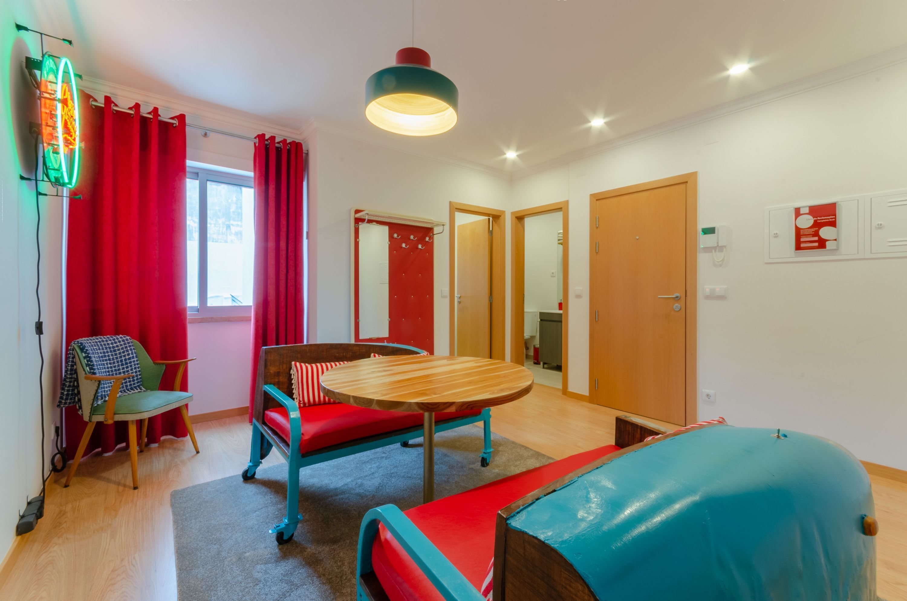 A room with a wooden table, red and blue furniture, a red curtain, and a neon light.