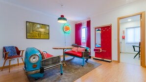 Quarto com um carro azul antigo, um sofá vermelho, uma pequena mesa e um letreiro neon.