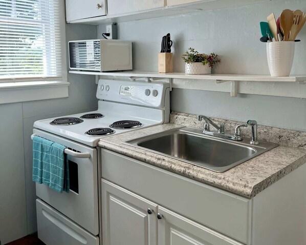 A kitchen with a white stove, a sink, and a countertop. - Crestview Cottage For 2 (St. Augustine)