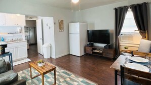 Un espace de vie compact comprenant un coin cuisine, un coin repas, un coin salon avec un canapé et une table basse, et un téléviseur.