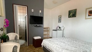 A hotel room with a bed, a desk with a chair, a television, and a small table with a plant. - Pousada Zenite (Natal)