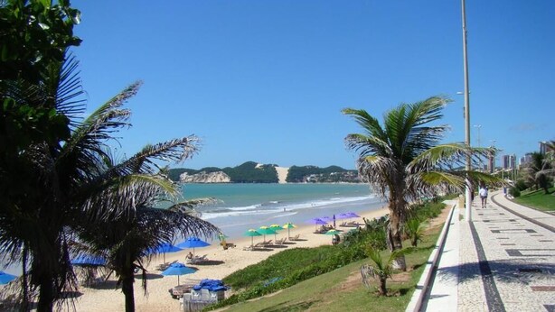 A beach with palm trees, umbrellas, and a paved walkway. - Pousada Zenite (Natal)