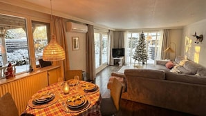 A cozy living room with a dining area, a sofa, a TV, and a Christmas tree.