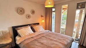 A bedroom with a bed, a chair, a hanging light fixture, and a view of the outdoors.