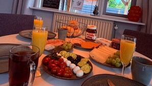 A breakfast table with a variety of foods, including cheese, tomatoes, cucumbers, and bread, along with drinks and condiments.