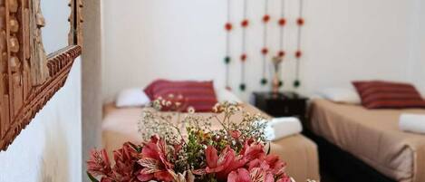 A wooden table with a floral arrangement in a room with two beds, a hanging light fixture, and a wall-mounted decoration.