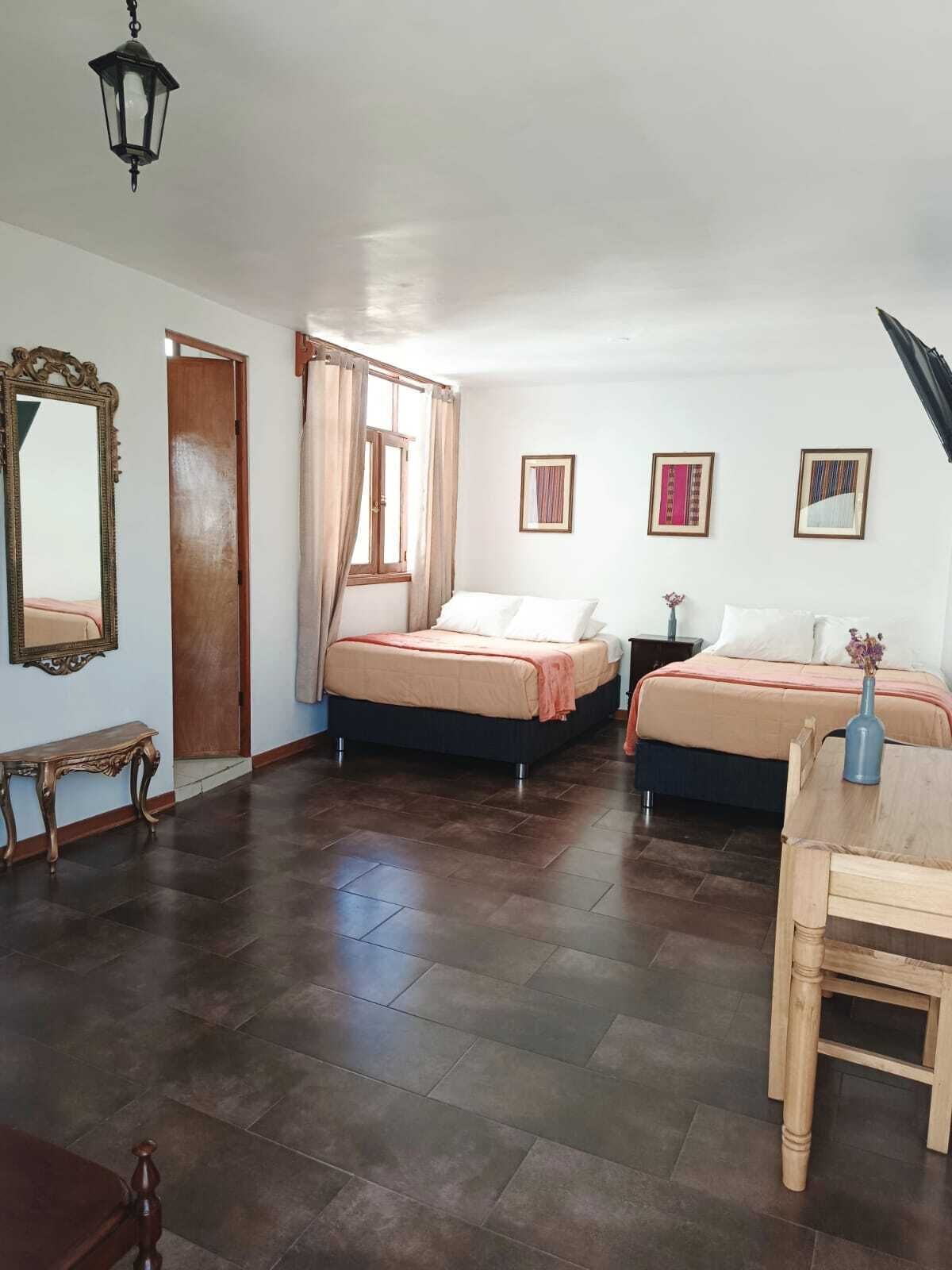 A room with two beds, a wooden table, a bench, and a mirror.