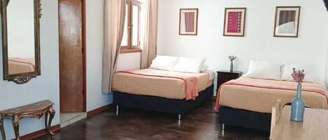 Una habitación con dos camas, una mesa de madera, un banco y un espejo.