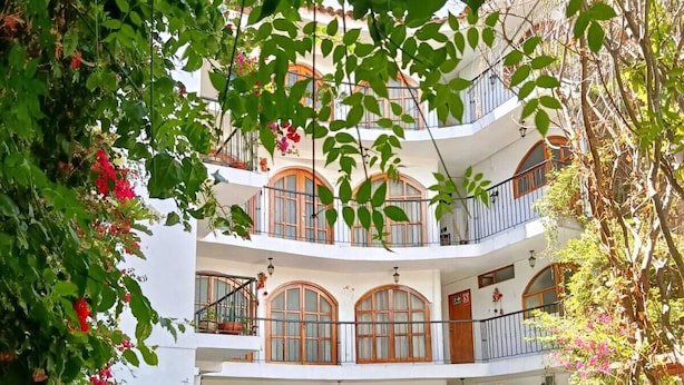 Un edificio de varios pisos con un patio que incluye asientos al aire libre y abundante vegetación.