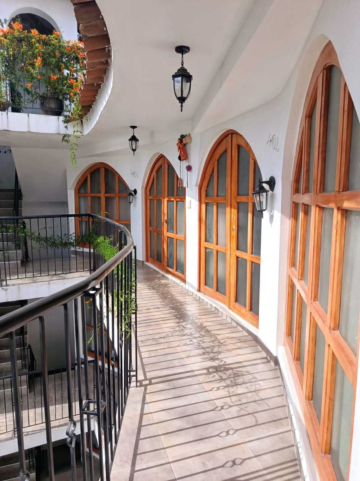 A covered corridor with wooden-framed windows, a tiled floor, and hanging plants.