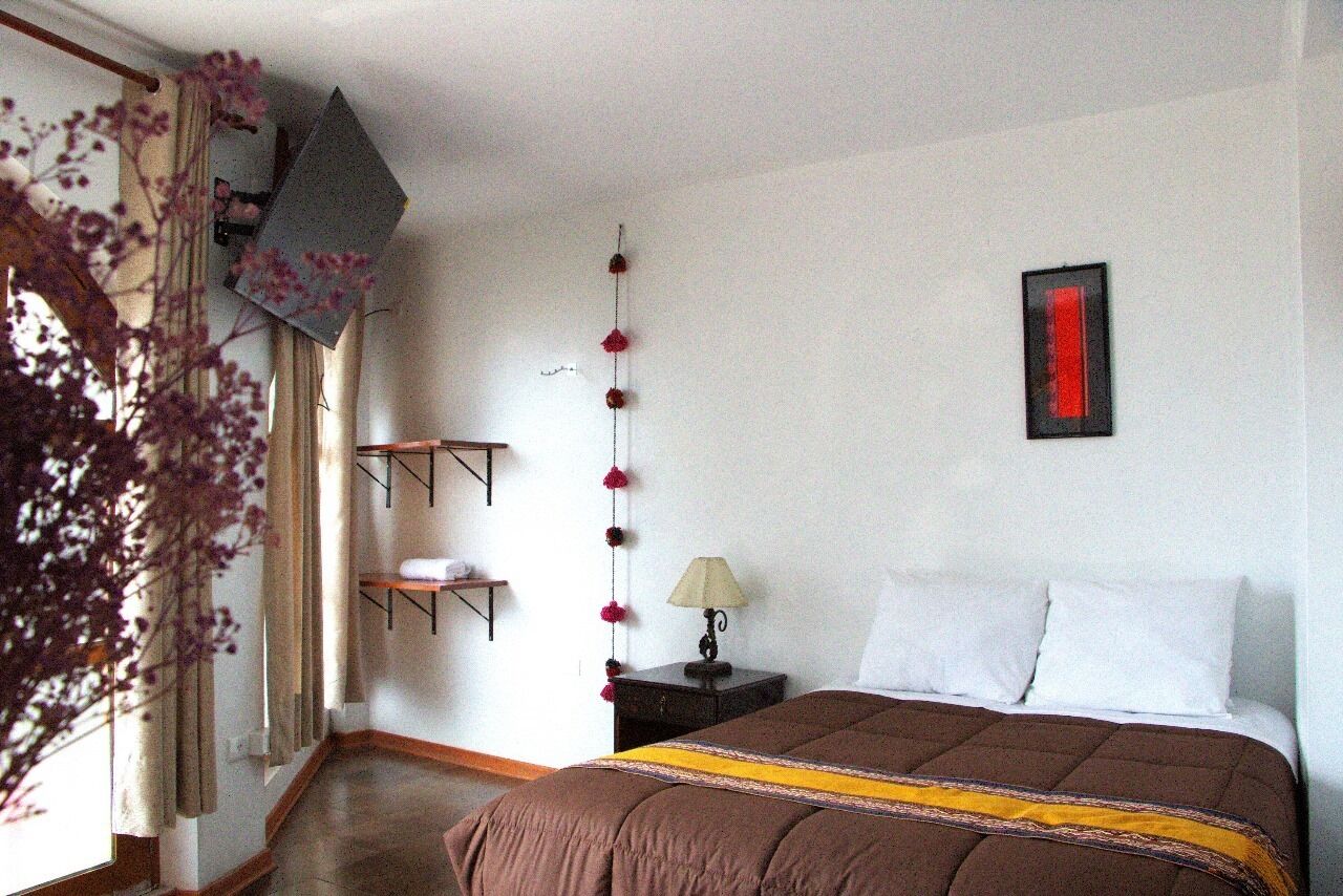 Un dormitorio con una cama, una mesita de noche, una lámpara, un estante en la pared y una guirnalda decorativa de flores.