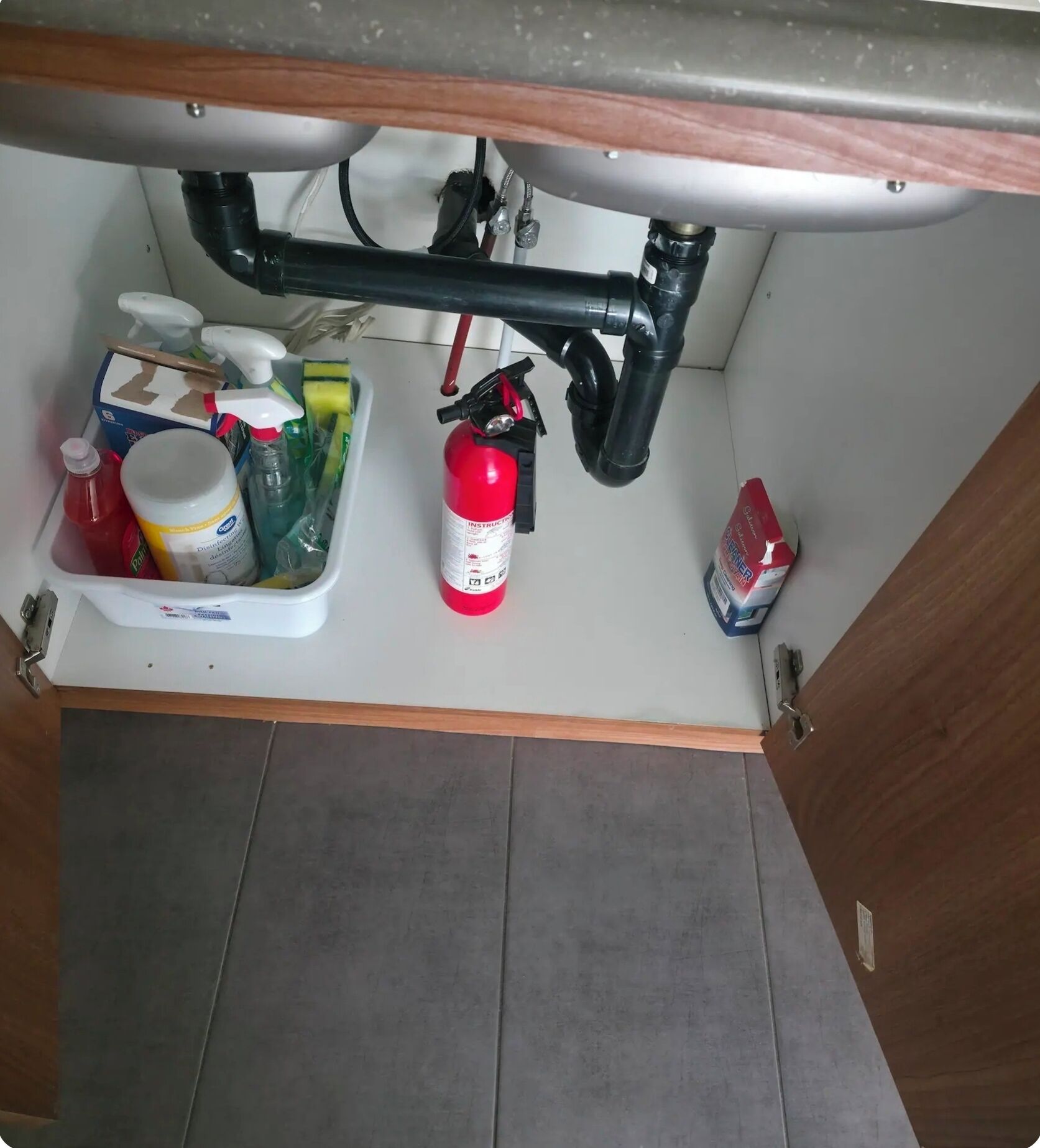 A kitchen with a white countertop, a sink, and various cleaning supplies including a red fire extinguisher, a bottle of dish soap, and a sponge.