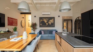 A modern kitchen with a central island, a dining area with a wooden table and chairs, and a blue sofa in the background. - THE BREAK - CAMPO MARZIO MAISON DELUXE (Roma)