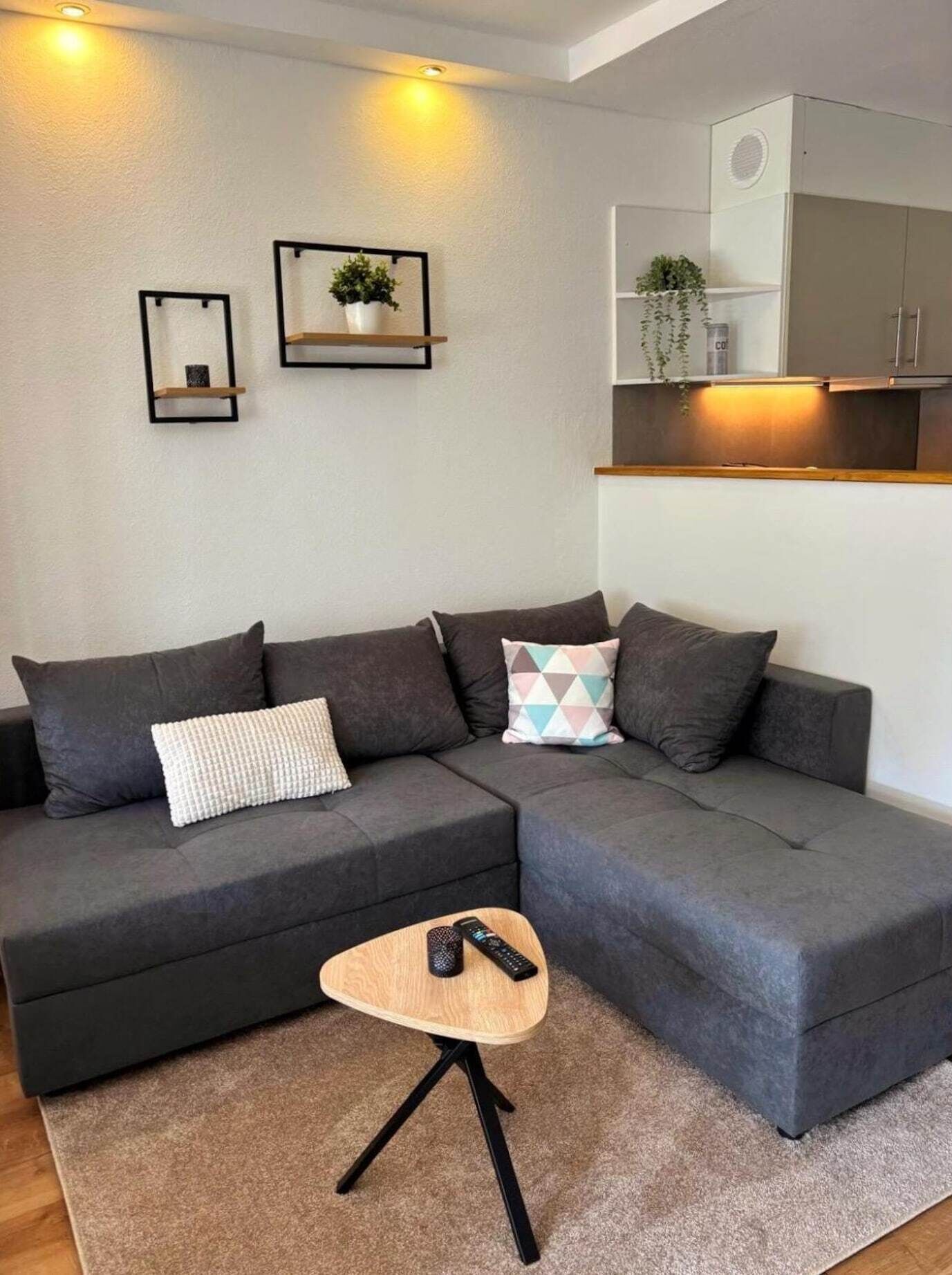 A modern living room with a sectional sofa, a small wooden side table, and a remote control on it.