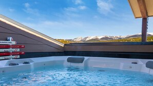 Ein Whirlpool mit Blick auf die Berge, umgeben von einer Holzterrasse und einem überdachten Bereich mit Beschilderung.