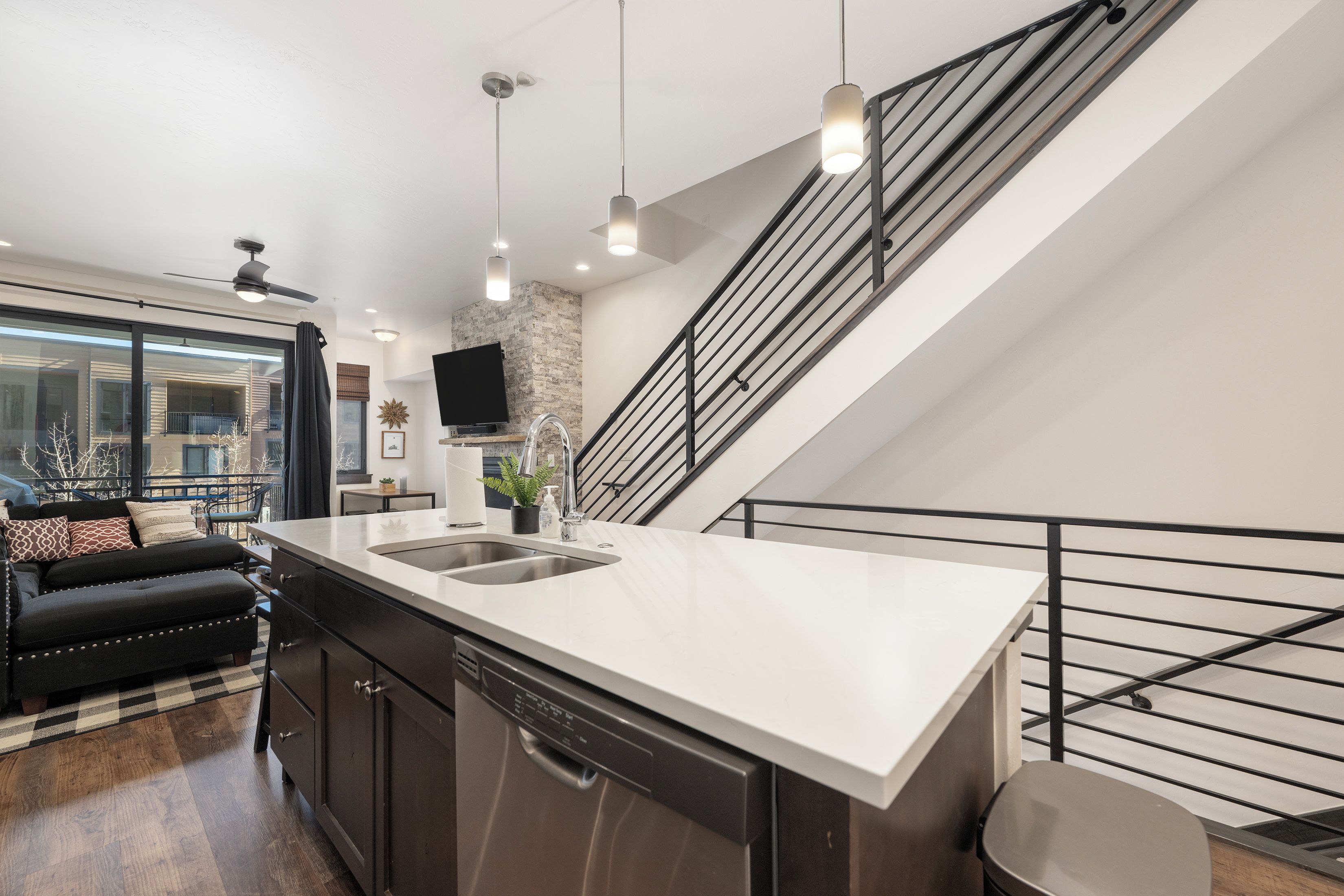 A modern kitchen with a dishwasher, a large island with a sink, and a staircase with a railing.