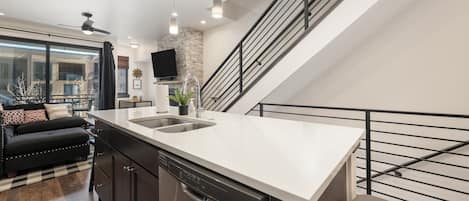A modern kitchen with a dishwasher, a large island with a sink, and a staircase with a railing.