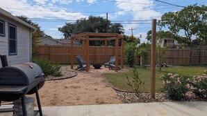 A backyard with a barbecue grill, a wooden pergola, and outdoor seating. - Sparkling City Stay S (Corpus Christi)