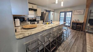 A modern kitchen with a marble countertop, stainless steel appliances, and a bar area with stools. - Sparkling City Stay S (Corpus Christi)