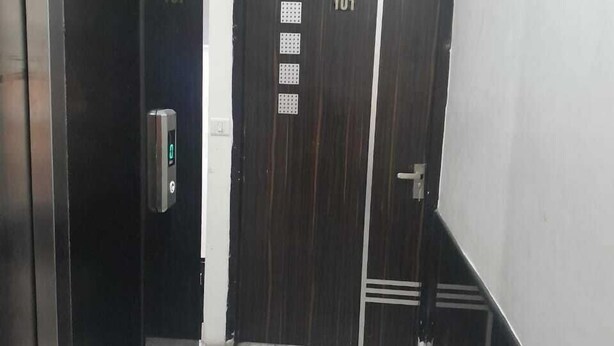 Un couloir au sol de marbre menant à une porte en bois sombre, portant le numéro 101.