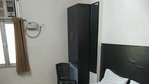 Un lit simple avec une couvre-lit à motifs, une armoire noire, une chaise et une fenêtre avec des rideaux.
