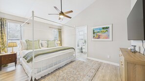 A bedroom with a four-poster bed, a ceiling fan, a television, and a painting on the wall.