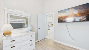 A room with a white dresser, a mirror, a lamp, and a painting of a waterfall.