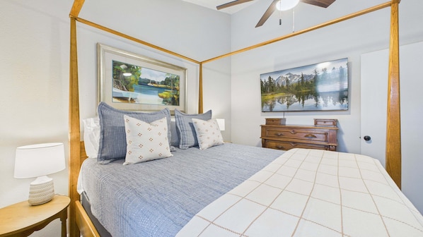 A bedroom with a four-poster bed, a dresser, a painting, and a lamp.