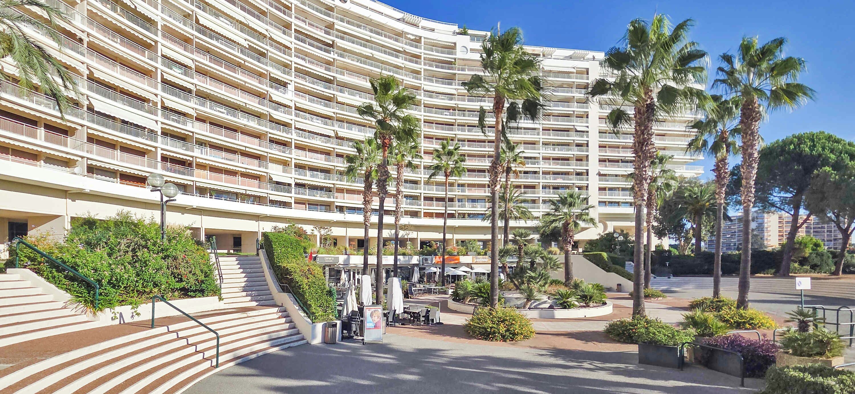 Un hotel a più piani con facciata curva, area salotto all'aperto, palme e una scalinata centrale.