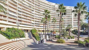 Un hotel a più piani con facciata curva, area salotto all'aperto, palme e una scalinata centrale.