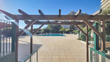 Estrutura de pérgola de madeira com um pátio ladrilhado que dá para uma piscina.