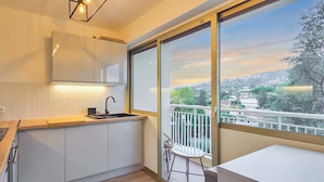 Eine moderne Küche mit weißen Schränken, einer Holzarbeitsplatte und einem großen Fenster mit Blick auf eine Stadtlandschaft und Hügel.