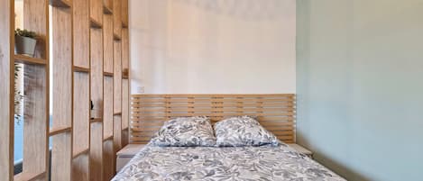 A bedroom with a wooden headboard, a bed with floral-patterned bedding, and a built-in wooden shelving unit with plants.