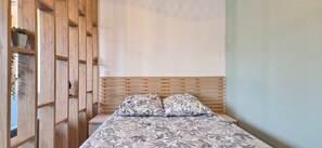 Una camera da letto con una testiera in legno, un letto con biancheria da letto a motivi floreali e una libreria a incasso in legno con piante.