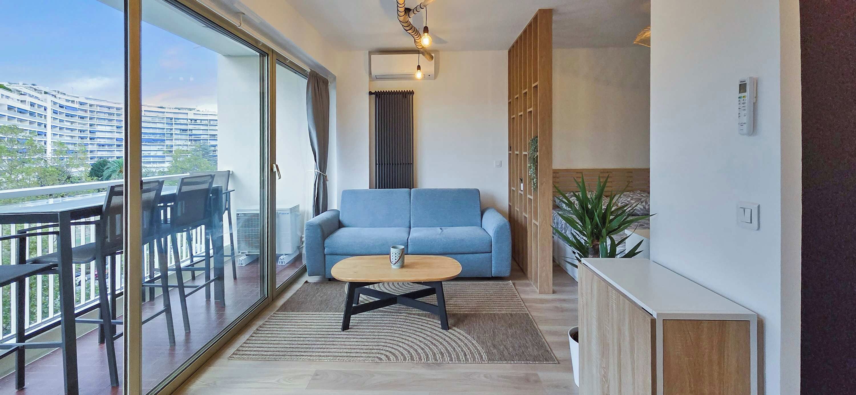 Uma sala de estar moderna com um sofá azul, uma mesa de centro de madeira e uma janela grande com vista para a cidade.