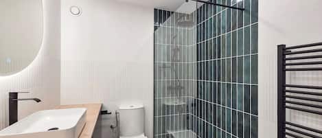 Uma casa de banho moderna com uma pia branca, sanita e zona de duche com parede de vidro.