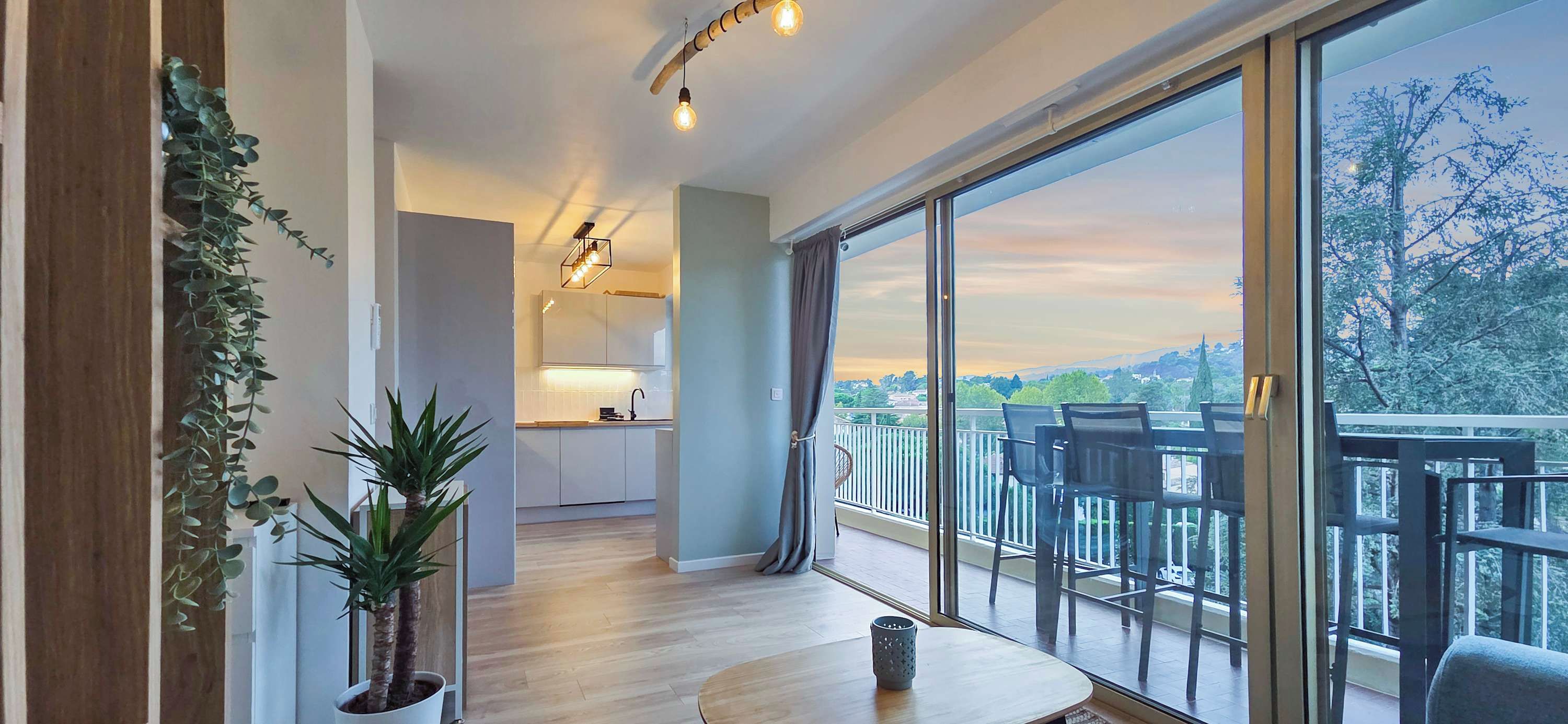 Ein modernes Apartment mit Küche, einem Balkon mit Stühlen und großen Fenstern mit Blick auf die Stadt.