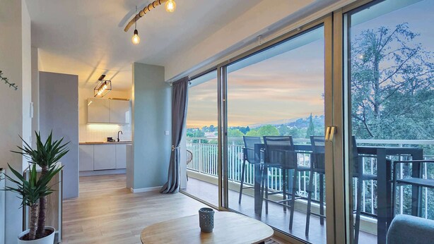 Ein modernes Apartment mit Küche, einem Balkon mit Stühlen und großen Fenstern mit Blick auf die Stadt.