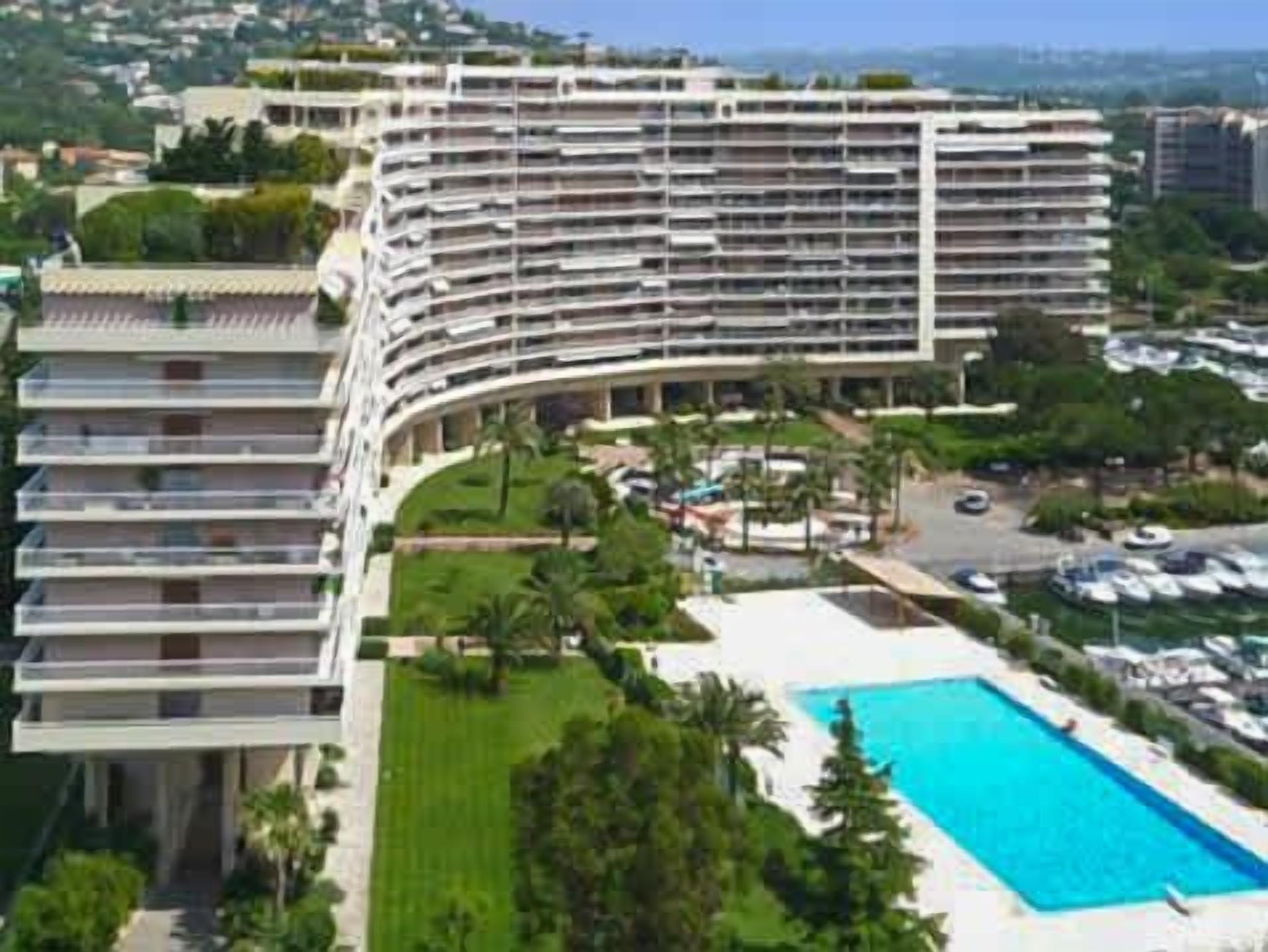 Um hotel com vários andares, fachada curva, piscina e área de jardim ajardinada.