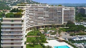 Ein mehrstöckiges Hotel mit geschwungener Fassade, einem Schwimmbad und einem angelegten Garten.