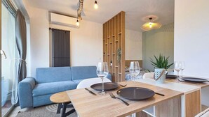 Ein modernes Wohnzimmer mit einem blauen Sofa, einem Holzesstisch, der mit Tellern, Weingläsern und Besteck gedeckt ist. Auf dem Tisch steht eine Pflanze und im Hintergrund ein Holztrenner.