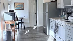 Moderni keittiö, jossa on valkoiset kaapit, ruostumattomasta teräksestä valmistettu jääkaappi, liesi sekä ruokailutila, jossa on pöytä ja tuolit.